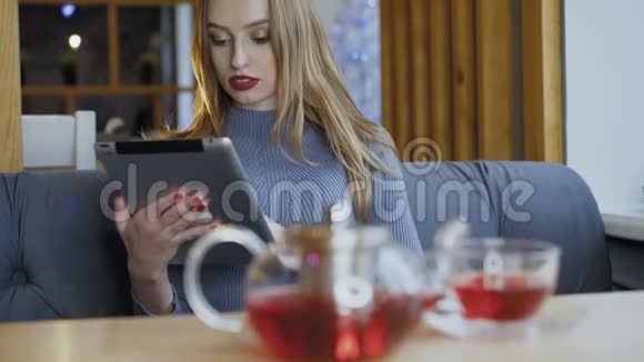 快乐的年轻女子喝茶微笑着使用平板电脑视频的预览图
