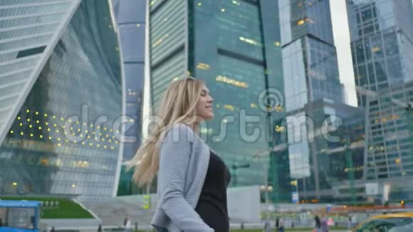 这个金发女孩在摩天大楼和城市高层建筑的背景下向相机发送一个空中吻视频的预览图