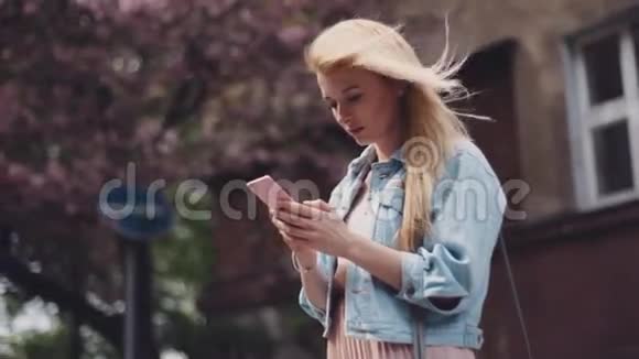城市里的风天气年轻的女人在用她的手机背景上的樱桃开花和路标视频的预览图