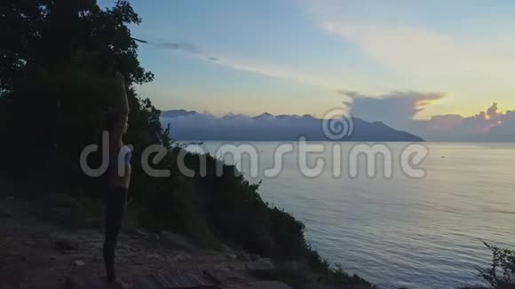 女孩做瑜伽纳马斯特阿萨纳双手在岩石海滩上的头上视频的预览图