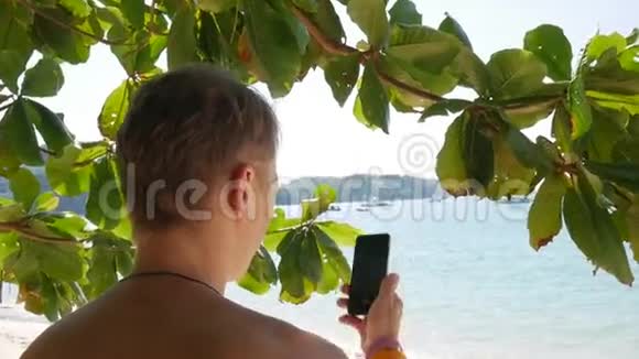 年轻人在海滩上使用智能手机拍摄惊人平静的蓝色海水高清慢运动泰国普吉岛视频的预览图