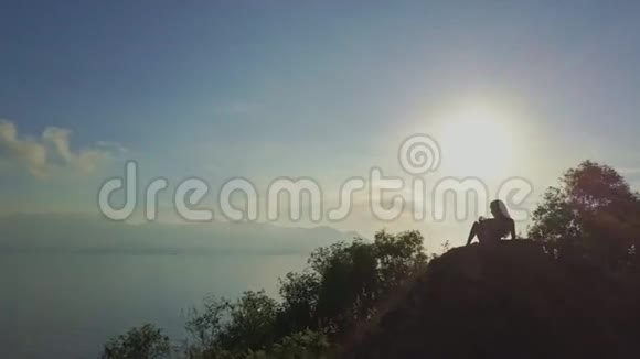 无人机在海边的悬崖边放松围绕着女孩的剪影视频的预览图