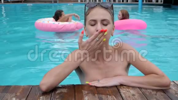 女孩在泳池里用粉色充气戒指亲吻背景女孩朋友游进游泳池视频的预览图