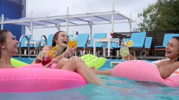 嘲笑坐在泳池充气圈的女孩夏天休息的朋友穿泳衣在游泳池鸡尾酒会视频的预览图