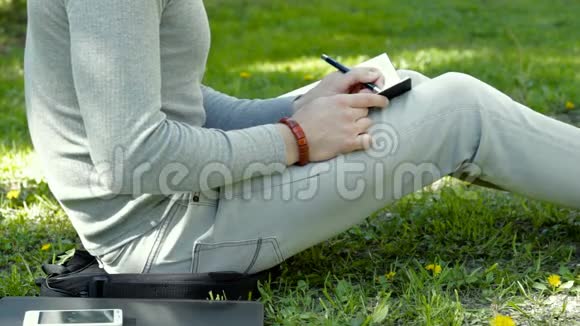 他坐在公园的草地上在笔记本上做记录视频的预览图