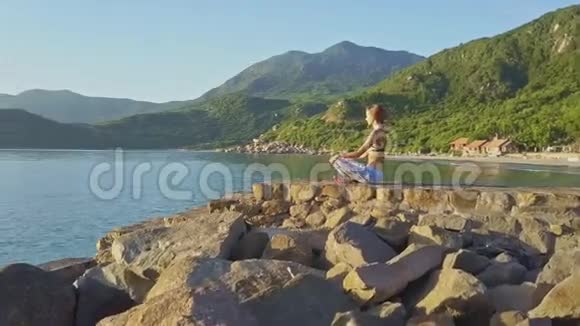 年轻的金发女孩坐在瑜伽筒里对抗丘陵景观视频的预览图