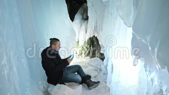 人类坐在冰洞里的平板电脑上围绕着神秘美丽的冰窟用户在视频的预览图