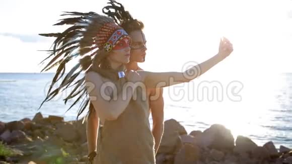 年轻的微笑美国土著男女穿着波希米亚风格的太阳服日落时在海边自拍视频的预览图