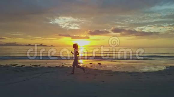 女孩剪影沿着海滩奔跑对抗上升的太阳之路视频的预览图