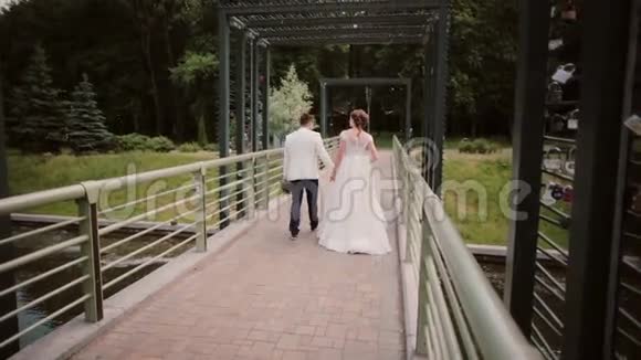 在公园的桥上散步的情侣的后景新娘和新郎在他们的婚礼上玩得很开心视频的预览图