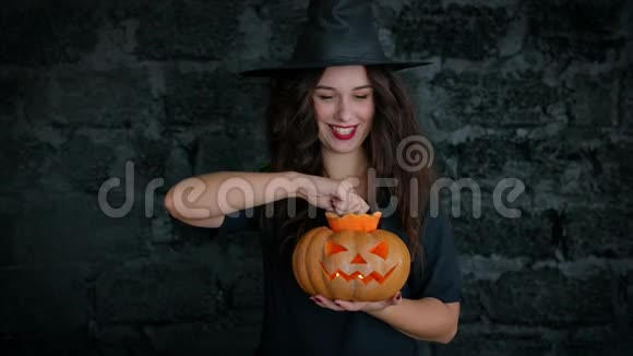 万圣节可爱的女孩表现出一个快乐的女巫她穿着一件黑色的连衣裙和帽子抱着南瓜的女孩视频的预览图