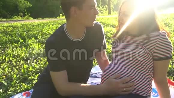 双手抚摸怀孕的肚子丈夫手抚摸着怀孕妻子的腹部柔和的夕阳照亮了视频的预览图