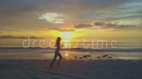 女孩的剪影在湿漉漉的沙滩上随着太阳的升起而慢跑视频的预览图
