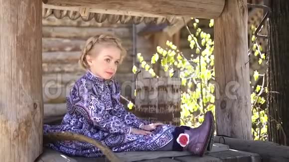 穿着传统服装的小漂亮女孩坐在一口古老的农村木井上的肖像全高清视频的预览图