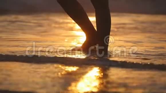 在日落时雌性的脚赤脚走在海边的海浪上日出时年轻女子沿海滩行走的腿视频的预览图