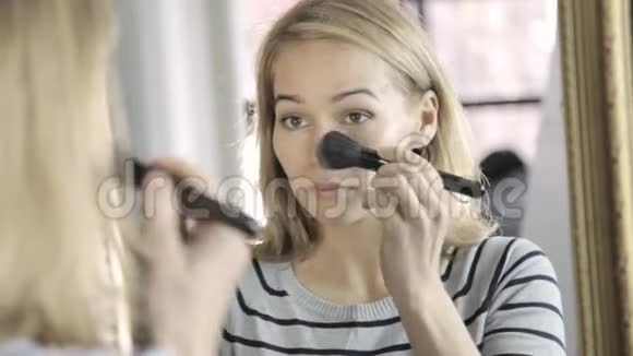 金发女人每天在镜子前化妆用刷子把粉涂在脸颊上视频的预览图