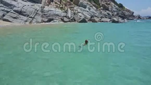 落基海滩附近的宁静的蔚蓝海洋中的女孩游泳视频的预览图
