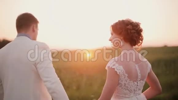 日落时分情侣们漫步在田野里愉快地享受着他们的婚礼新娘穿着漂亮的白色连衣裙视频的预览图