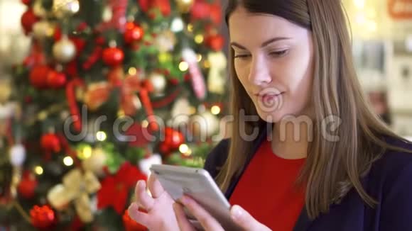 圣诞树附近的女人使用手机的漂亮女性在新年中获得祝贺视频的预览图