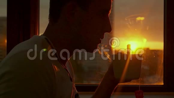 傍晚日落时分一个年轻人休息在窗边喝热茶高清1920x1080慢动作视频的预览图