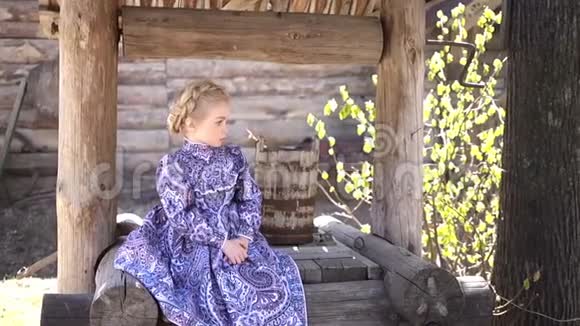 穿着传统服装的小漂亮女孩坐在一口古老的农村木井上的肖像全高清视频的预览图