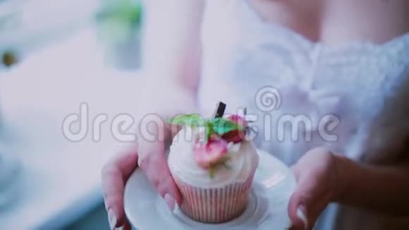 在茶托上近距离观看漂亮的纸杯蛋糕女人拿着一盘蛋糕闻着甜点的味道视频的预览图