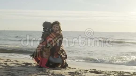 可爱的小男孩和他的母亲在海上有格子的女人拥抱她的儿子手牵着手海滩上的幸福家庭视频的预览图