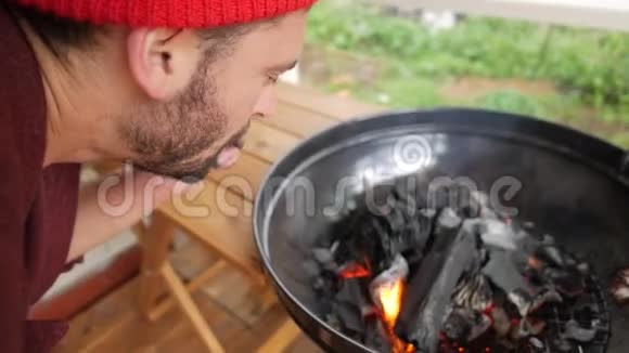 年轻的大胡子在烧烤炉里吹着煤火黑色木制木炭燃烧在Bbq高清高清视频的预览图