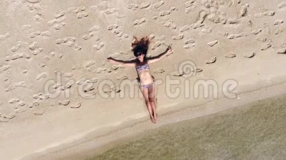 空中年轻美丽的微笑女人在比基尼躺在海滩上白人女性模特在海滩上洗澡苏视频的预览图