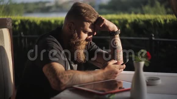 男人坐在自助餐厅或餐厅拿着智能手机看着它的屏幕使用小玩意的人视频的预览图