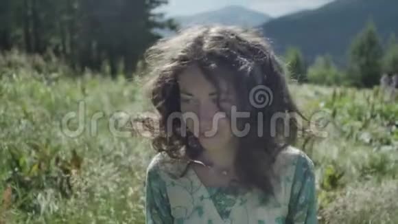 害羞的女孩看着相机微笑着在风的草地上视频的预览图