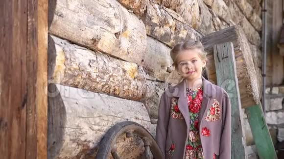 穿着传统服装站在老农村木屋前的小漂亮女孩的肖像全高清视频的预览图