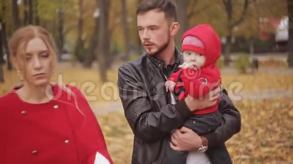 一个年轻的家庭带着婴儿车和婴儿漫步在秋天的公园里视频的预览图