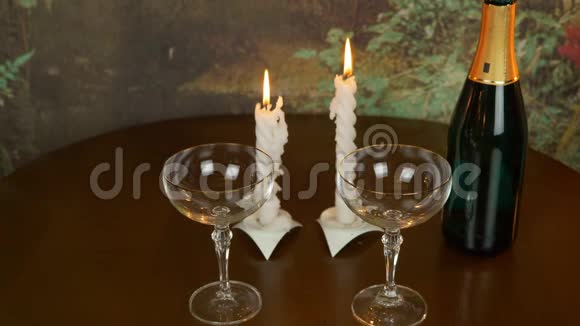 表暗木色两个空酒杯配对蜡烛照明吹蜡烛桌上放着一瓶香槟酒视频的预览图