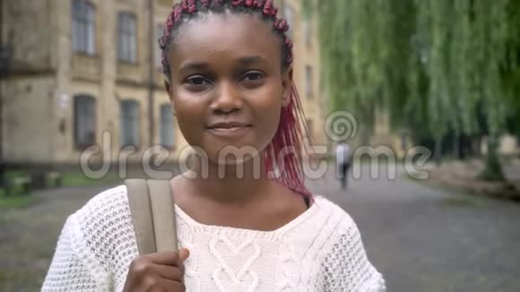 美丽快乐的非洲学生微笑着拿着背包站在大学附近公园的画像视频的预览图