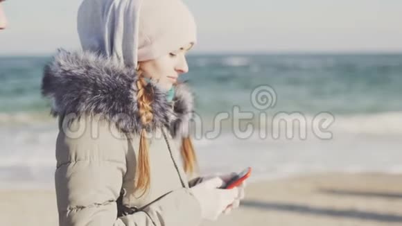 在寒冷的冬日一位拥有智能手机的女士在美丽的海滩上漫步视频的预览图