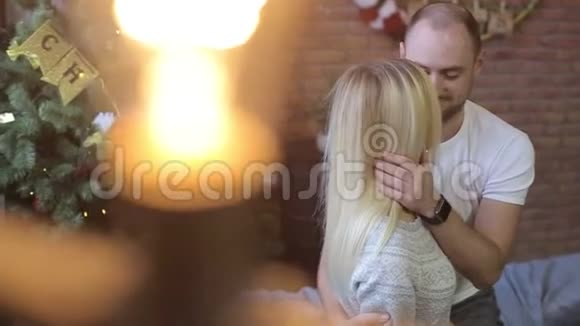 年轻夫妇坐在圣诞树背景上的床上在家过喜庆的夜晚男人亲吻女人视频的预览图