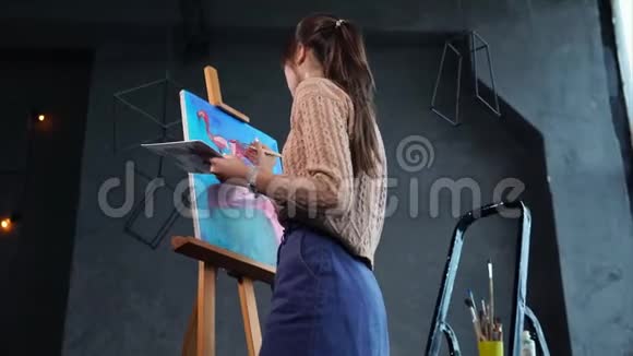 女孩用粉红色画火烈鸟画在画室的画架上视频的预览图