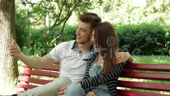 恋爱中的年轻夫妇在公园的长凳上自拍视频的预览图