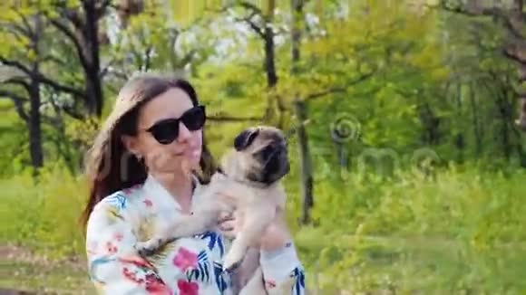 年轻时尚的女士戴着太阳镜在公园里和一只狗狗一起散步抱着一只宠物视频的预览图