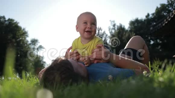 爸爸和可爱的蹒跚学步的儿子在公园草坪上放松视频的预览图
