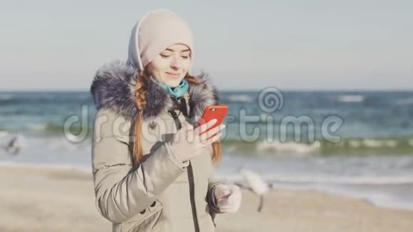在寒冷的冬日一位拥有智能手机的女士在美丽的海滩上漫步视频的预览图