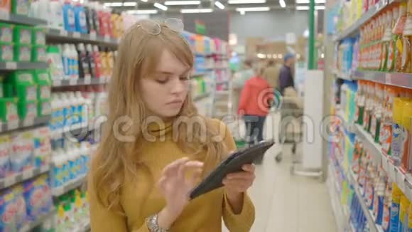 女性在超市购物并在平板电脑技术和零售概念上使用移动应用程序视频的预览图