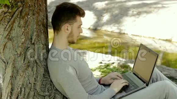 一个人坐在公园的树下拿着笔记本电脑工作视频的预览图