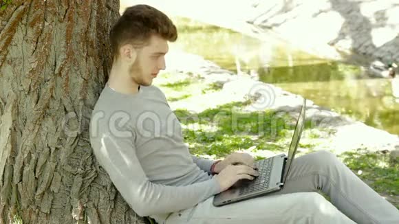 男人坐在树的阴影下手提电脑喝咖啡视频的预览图