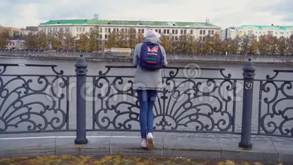 站在码头上的女孩穿暖和衣服的年轻女子站在码头的钢栏杆旁秋天的景色视频的预览图
