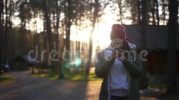 一个年轻的女孩正在拍摄一张照片背景是一个森林村庄和一个美丽的日落慢动作1920x1080满视频的预览图