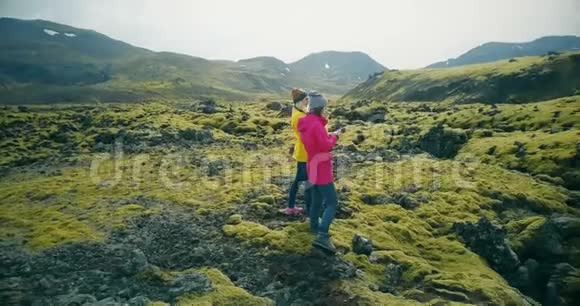 鸟瞰两名游客妇女在冰岛的熔岩上散步和拍照女孩使用智能手机和相机视频的预览图