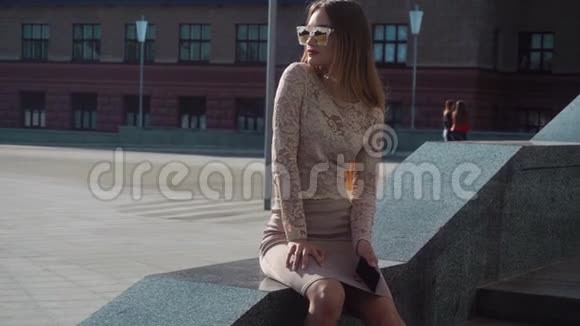 年轻的金发女孩戴着金色太阳镜坐在街上视频的预览图