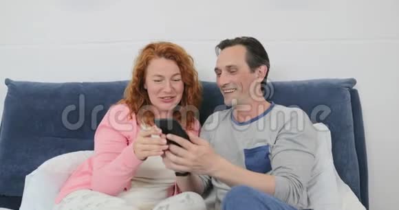 家庭在卧室里父母用手机而孩子们早上一起玩游戏视频的预览图